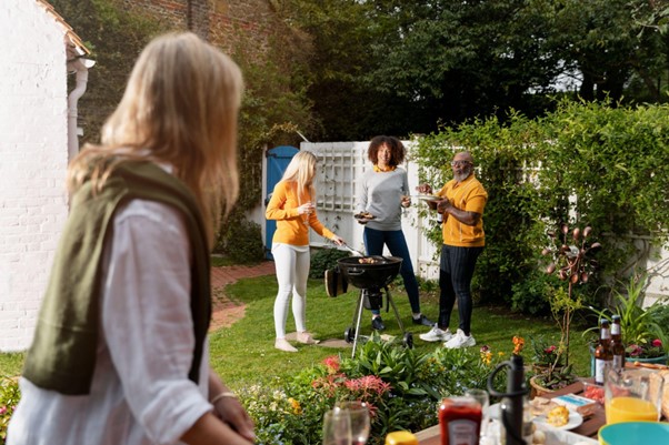 [Obrázok: Žena v popredí sa pozerá na svojich priateľov, ktorí si v záhrade užívajú grilovanie, zatiaľ čo jedna priateľka griluje a ostatní podávajú jedlo a nápoje. (freepik)]